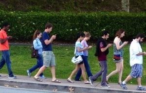 A group of teens all walking and staring down at their phones.
